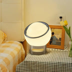 Clérachic table lamp lit on a checked bedside cloth, beside a framed picture, yellow tulips and a gingham bedspread.