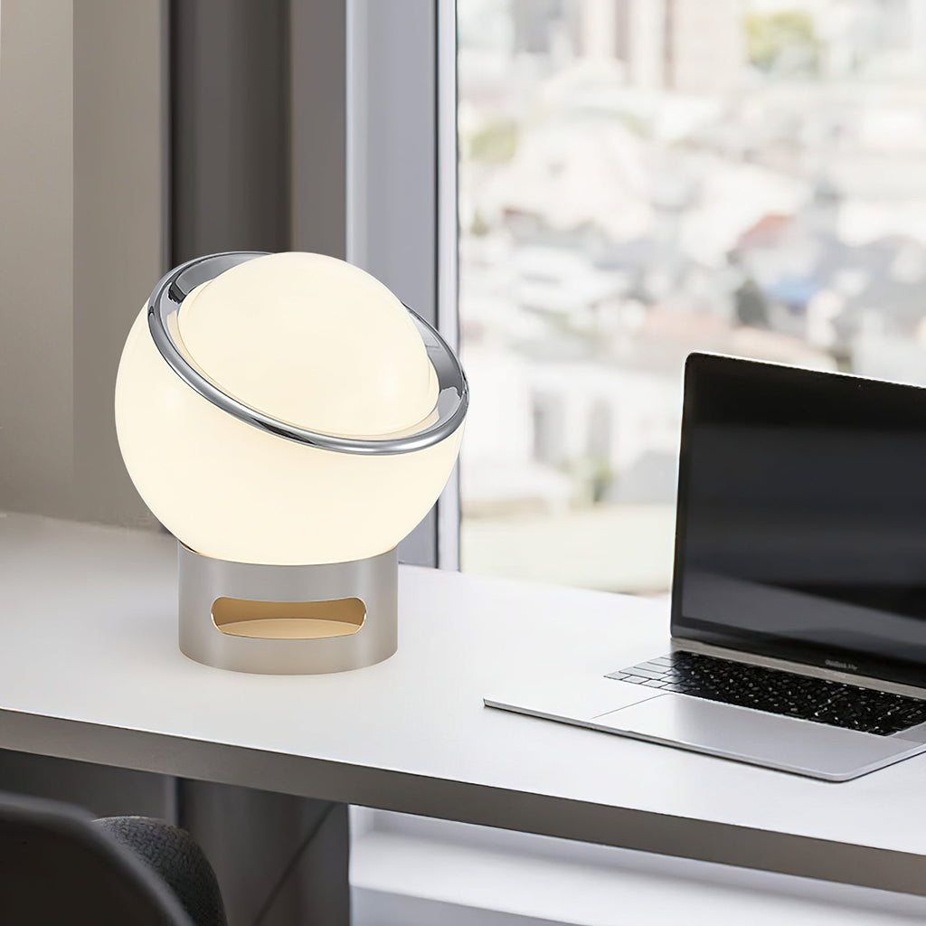 This Clérachic globe table lamp lit on a white desk beside an open laptop, with a city view through the window behind.