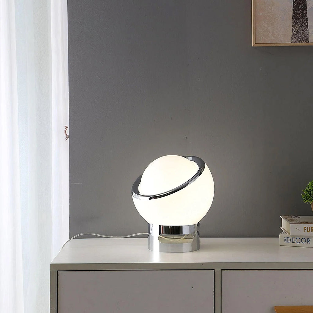 Clérachic table lamp with a white glass globe and chrome base on a white chest of drawers, with a curtain and books beside it.