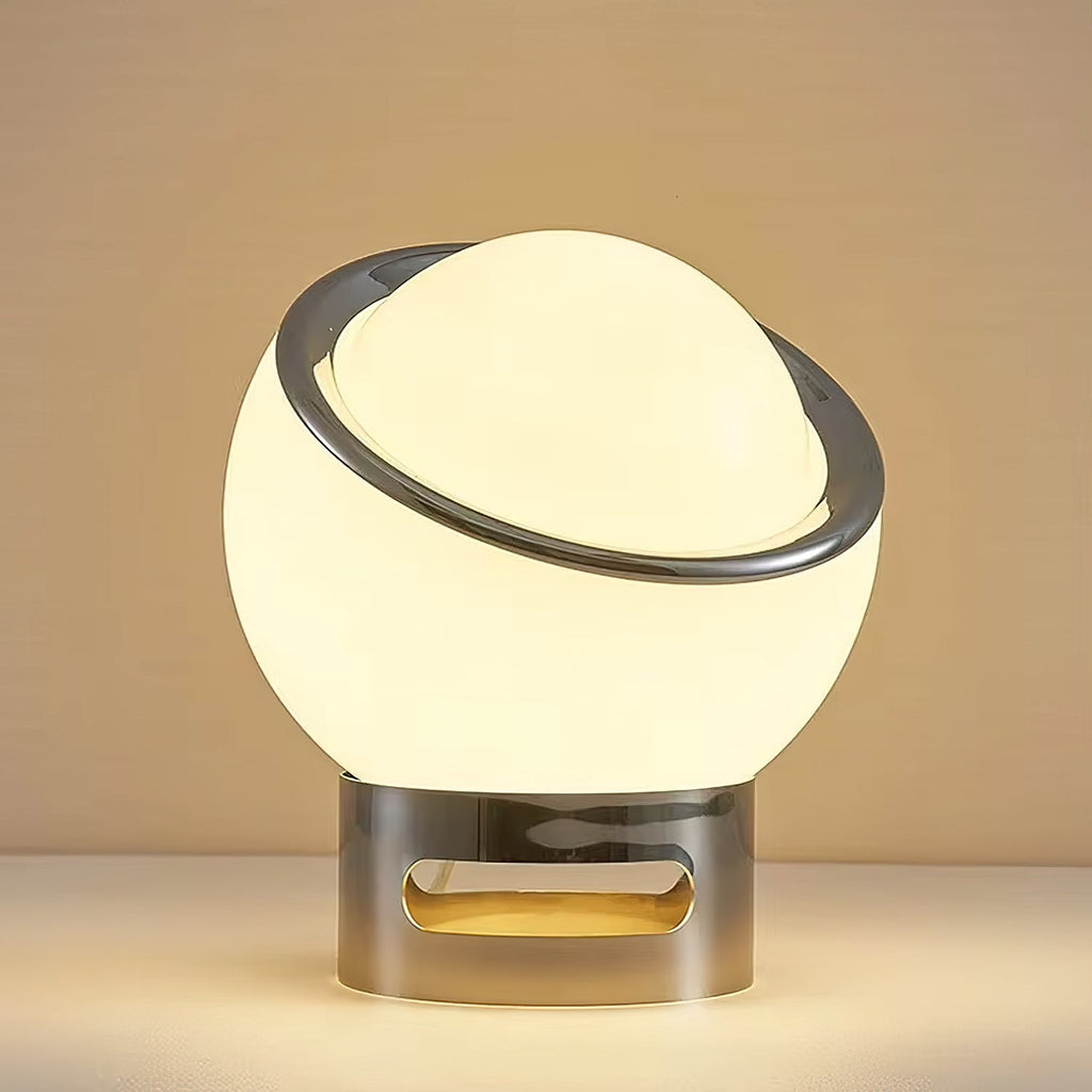 Close view of the lit white glass globe, polished chrome ring and slotted chrome base of this Clérachic table lamp on a warm backdrop.
