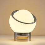 Close view of the lit white glass globe, polished chrome ring and slotted chrome base of this Clérachic table lamp on a warm backdrop.