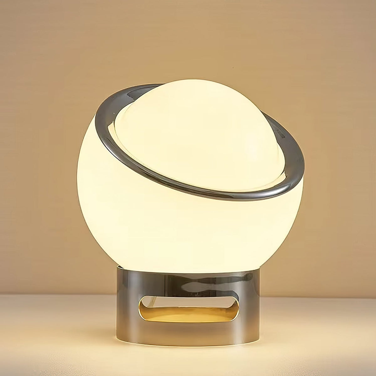 Close view of the lit white glass globe, polished chrome ring and slotted chrome base of this Clérachic table lamp on a warm backdrop.