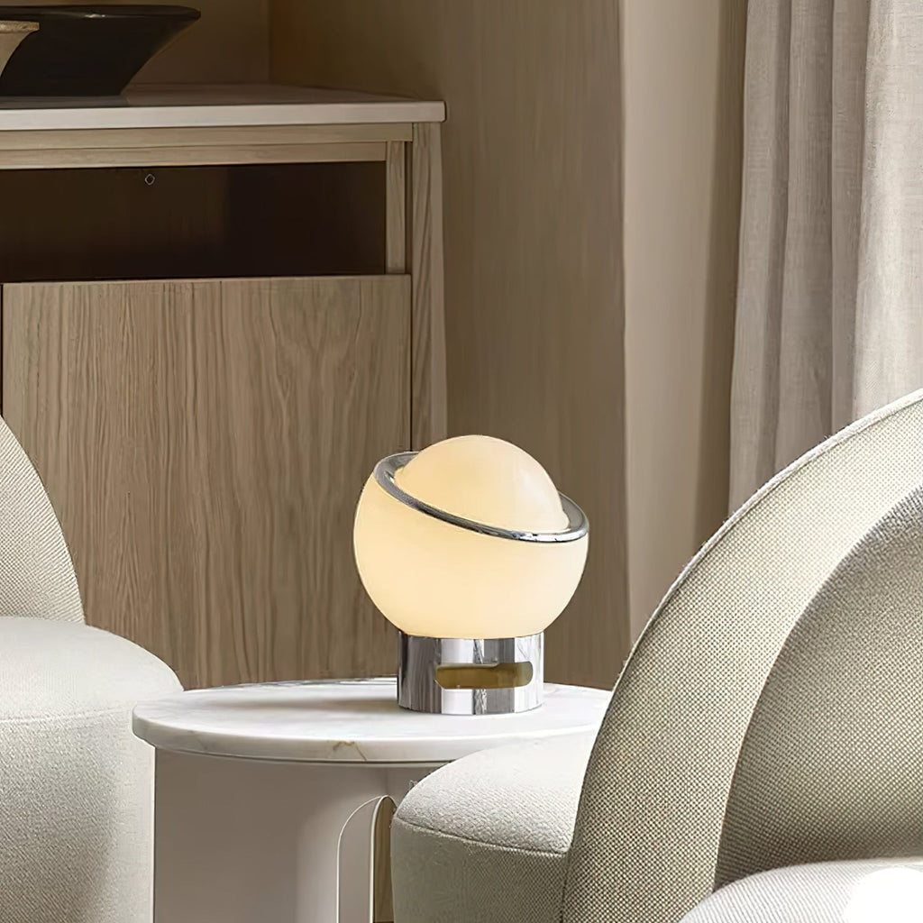 Lit white Clérachic table lamp on a round marble side table between two cream armchairs, with a wood-panelled wall behind.
