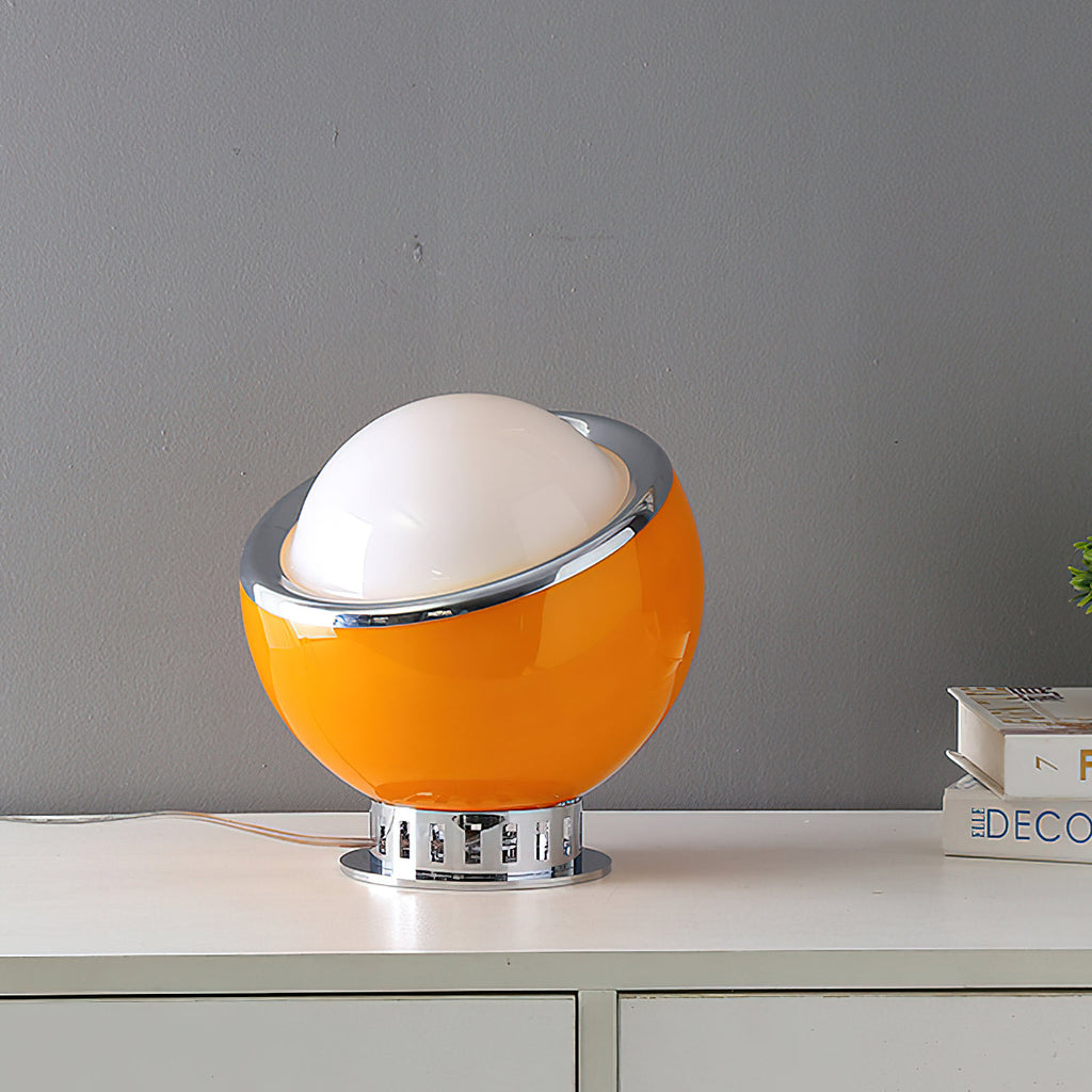 Orange Clérachic table lamp with an unlit white dome and a chrome ring, on a white cabinet beside a stack of books.