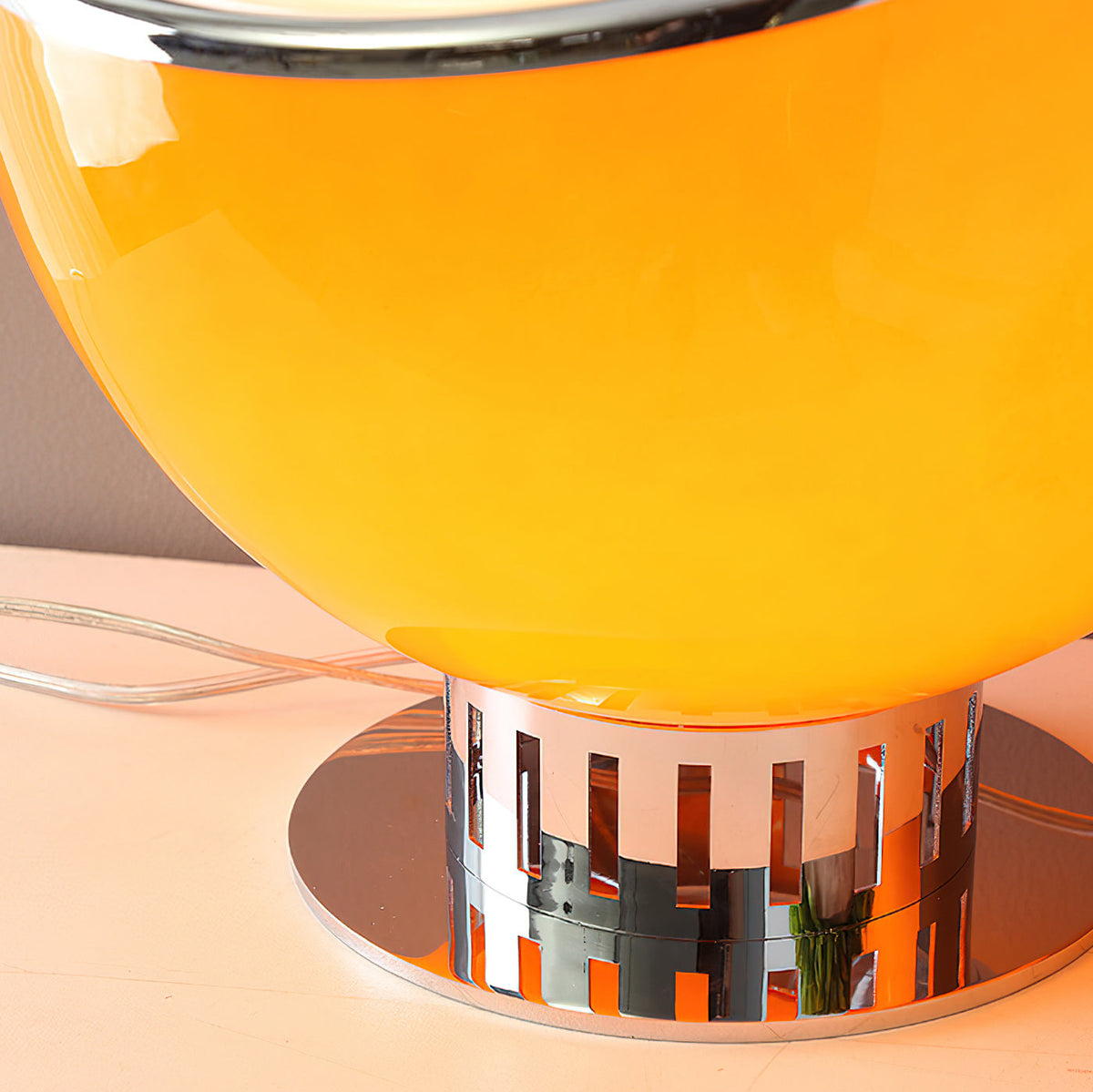 Close view of the slotted chrome base and round chrome plate under the orange globe of this Clérachic table lamp.