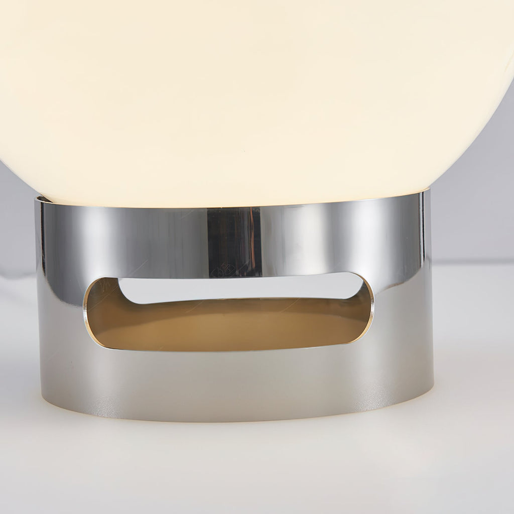 Close view of the chrome base with its oval cut-out, where the lit white globe of this Clérachic table lamp rests.