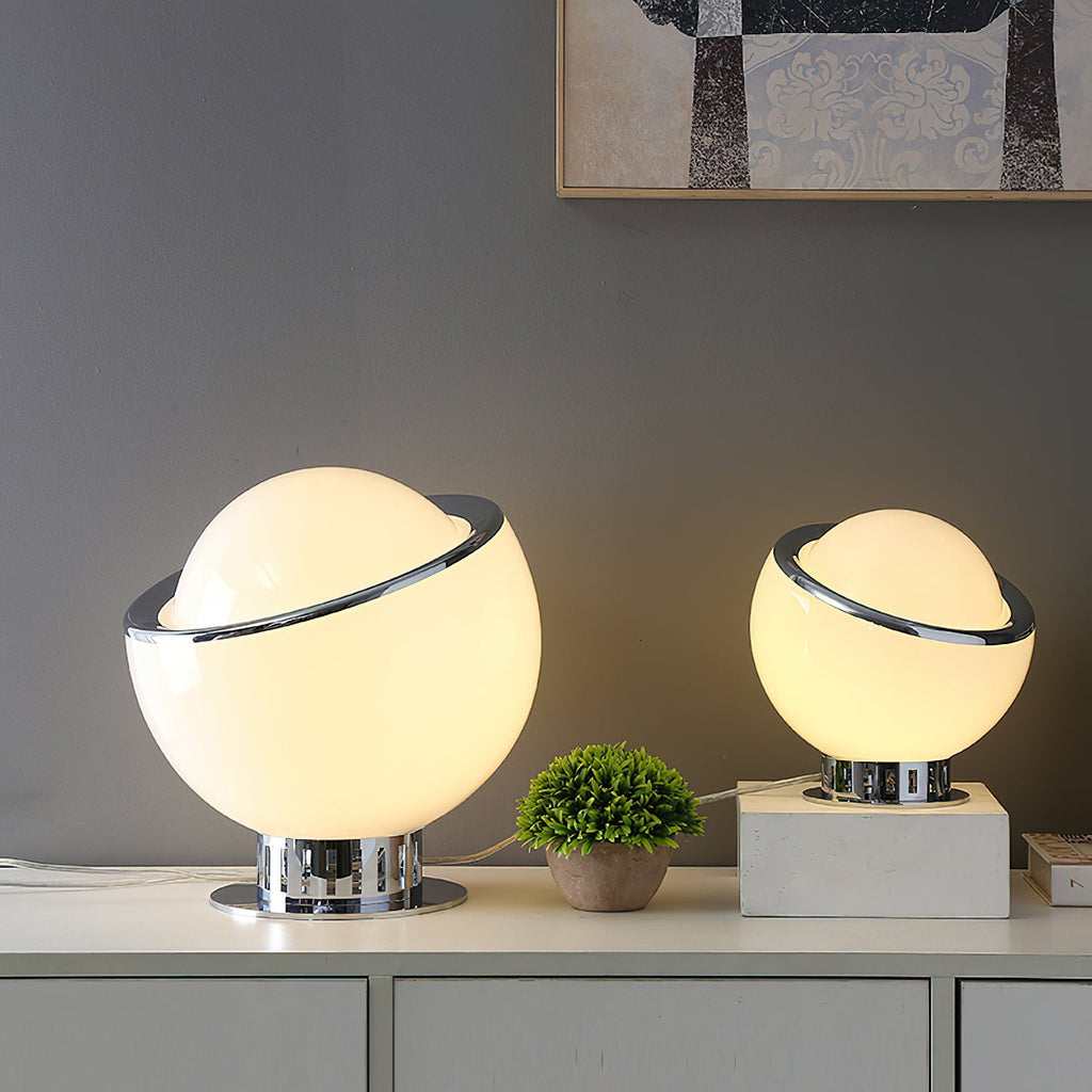 Two lit white Clérachic table lamps, one large and one small, on a white sideboard with a potted plant and a patterned picture above.