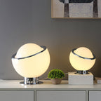 Two lit white Clérachic table lamps, one large and one small, on a white sideboard with a potted plant and a patterned picture above.