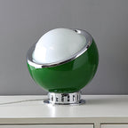 Green Clérachic table lamp with a white dome, chrome ring and ribbed chrome base, on a white cabinet against a grey wall.