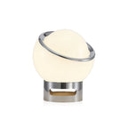 Lit white Clérachic table lamp with a tilted chrome ring and a chrome base with an oval cut-out, on a plain white backdrop.