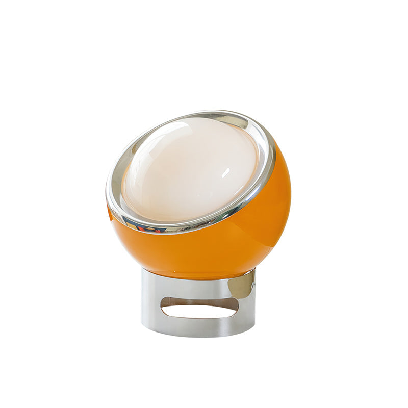 Orange Clérachic table lamp tilted on a chrome base with an oval cut-out, its white dome and chrome rim shown on a white backdrop.