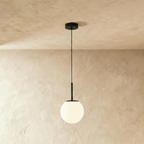 Clérachic Cells pendant light in Straight, Black, a matte black rod holding a frosted glass globe from a plaster ceiling.