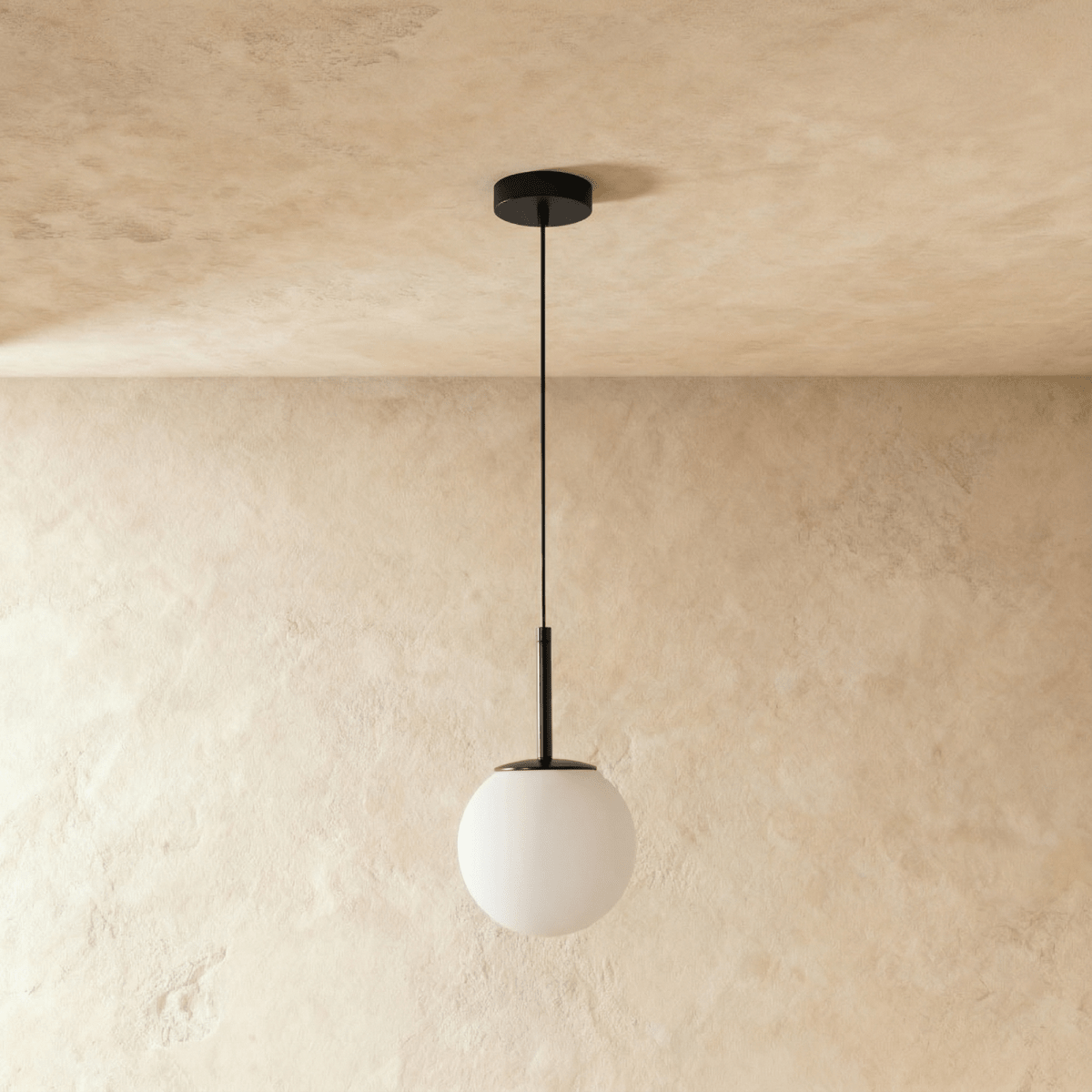 Clérachic Cells pendant light, Straight profile in Black, its frosted globe glowing softly against a warm plaster wall.
