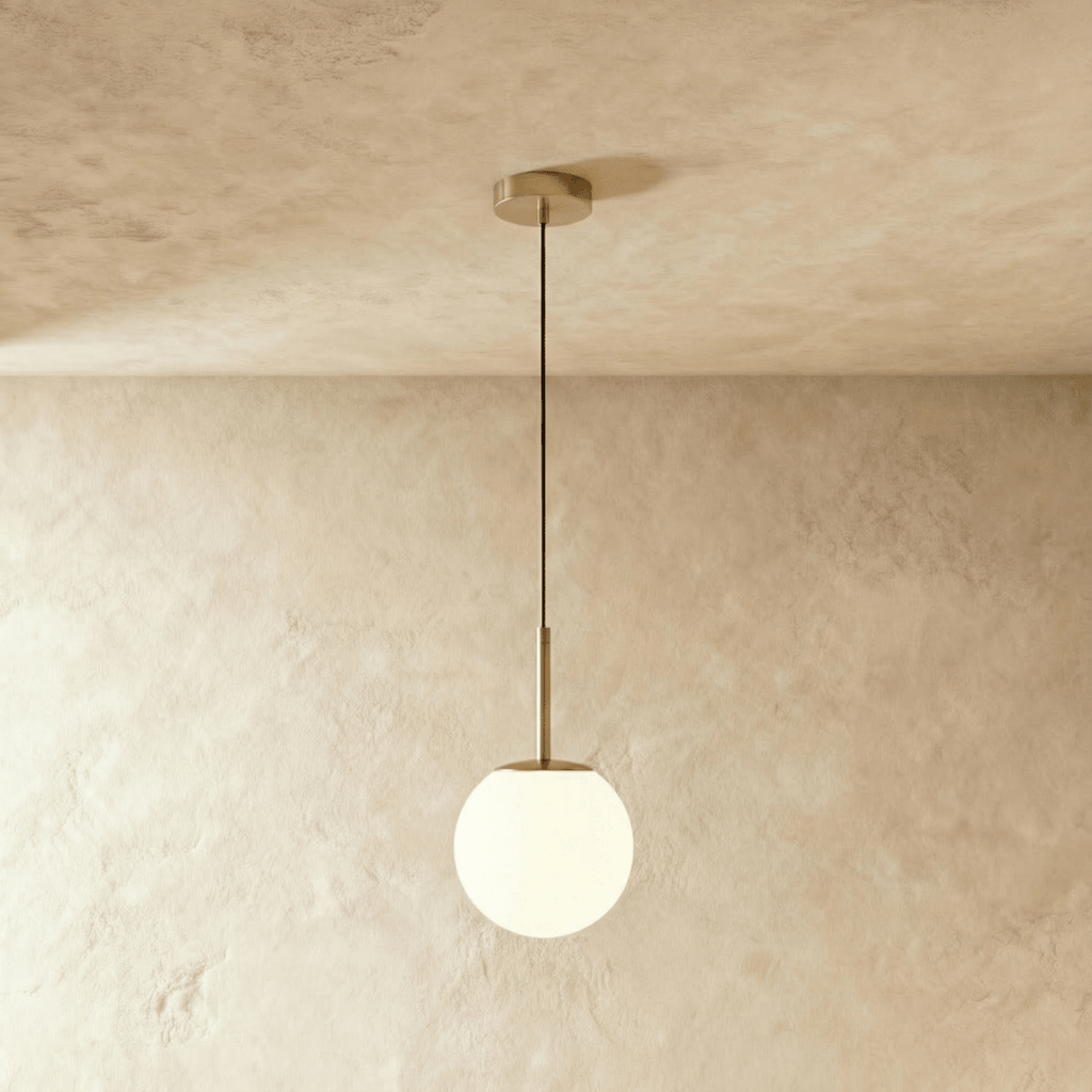 Clérachic Cells pendant light in Straight, Brass, a warm brass rod holding a frosted glass globe over a plaster wall.