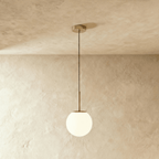 Clérachic Cells pendant light in Straight, Brass, a warm brass rod holding a frosted glass globe over a plaster wall.