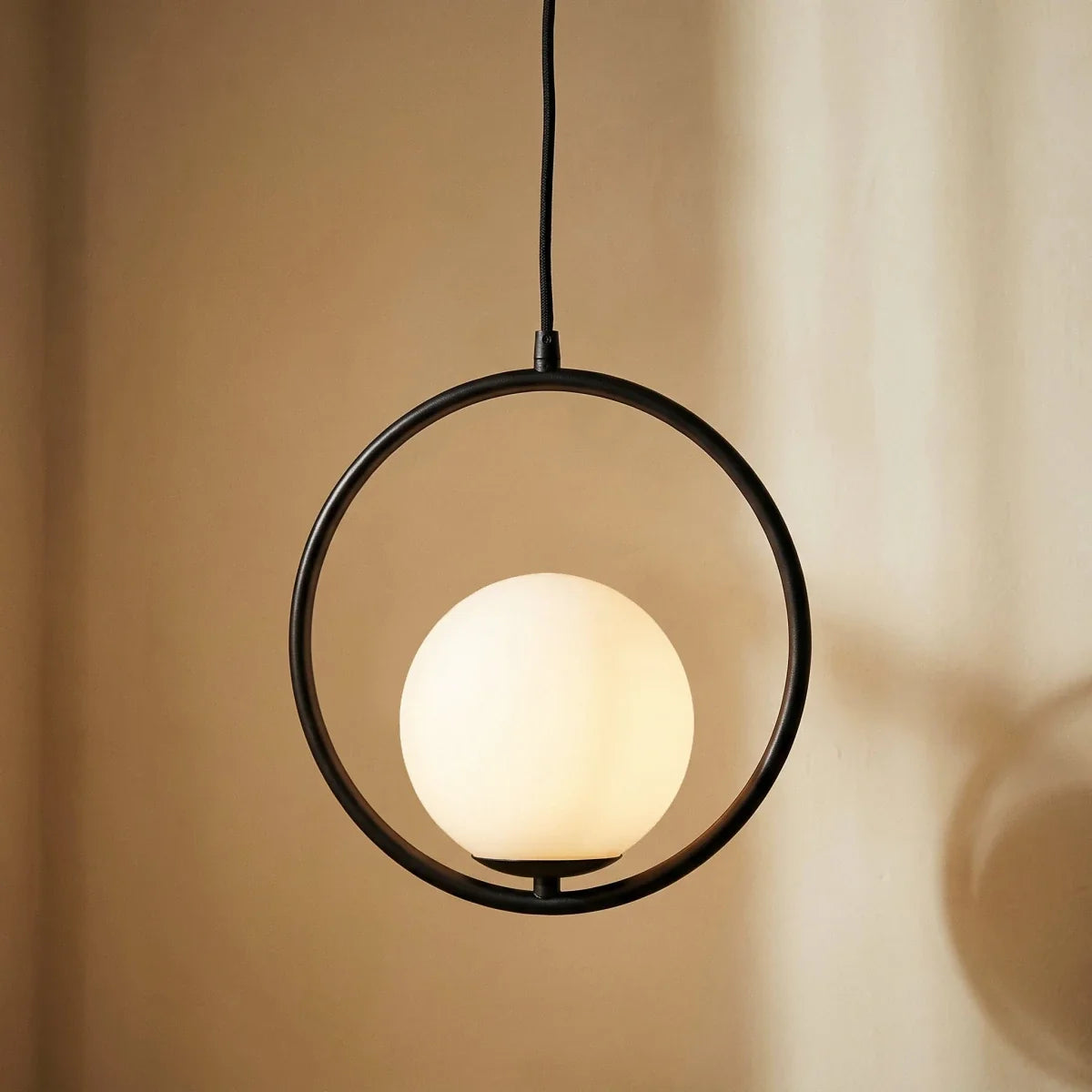 Close-up of the Clérachic Cells pendant light in Circle, Black, its frosted globe glowing warm inside the matte ring.