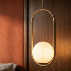 Close-up of the Clérachic Cells pendant light in Oval, Brass, its frosted globe lit warm inside the slim brass frame.