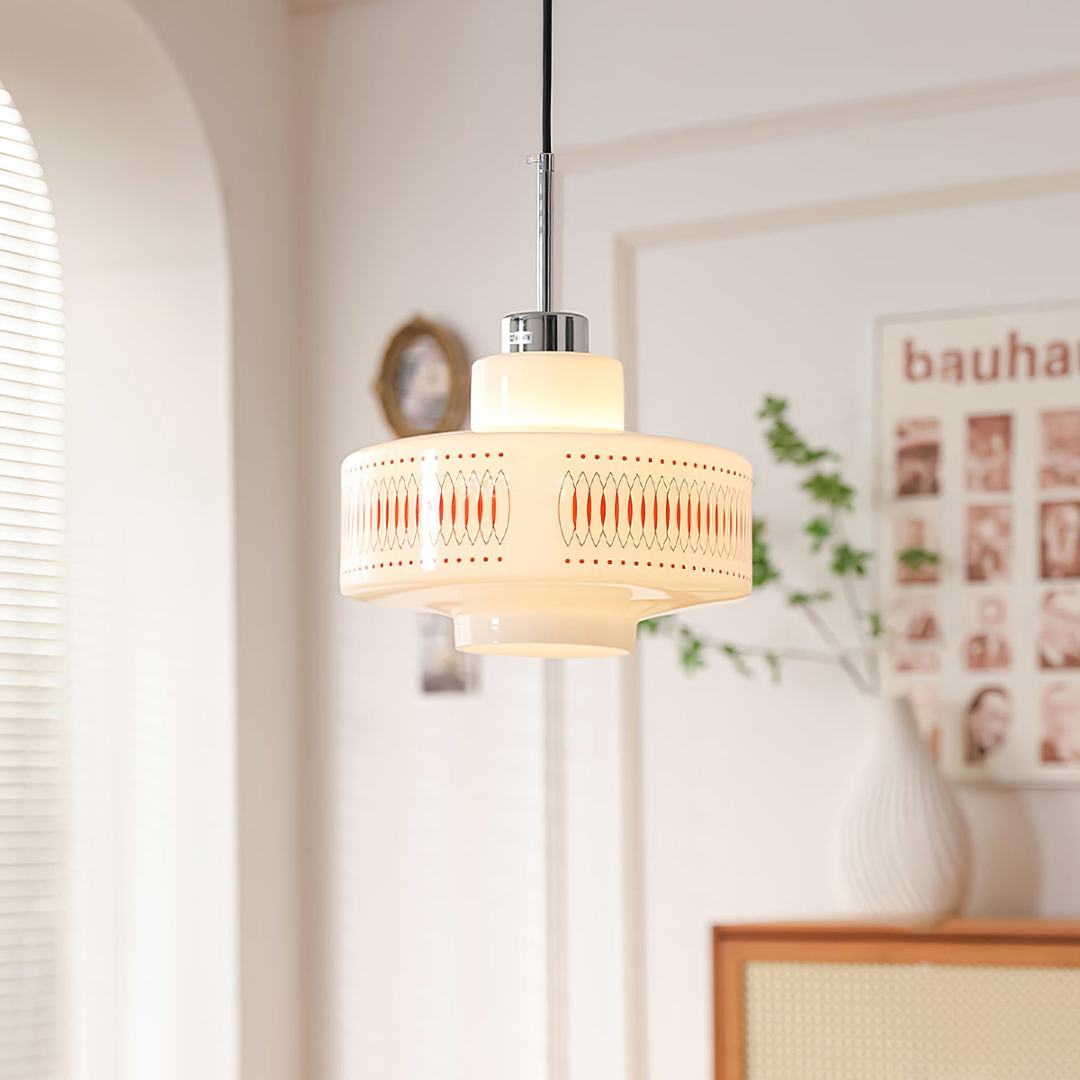 A Clérachic opal glass pendant with an orange lattice band glows beside a white vase, a rattan cabinet and an arched wall.