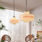Two Clérachic pendants of different sizes hang by a sheer-blinded window, with fan-back chairs and white flowers below.