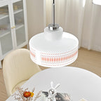 Low angle on a Clérachic pendant with a white drum shade and orange print, hanging above a white oval table and cream chair.