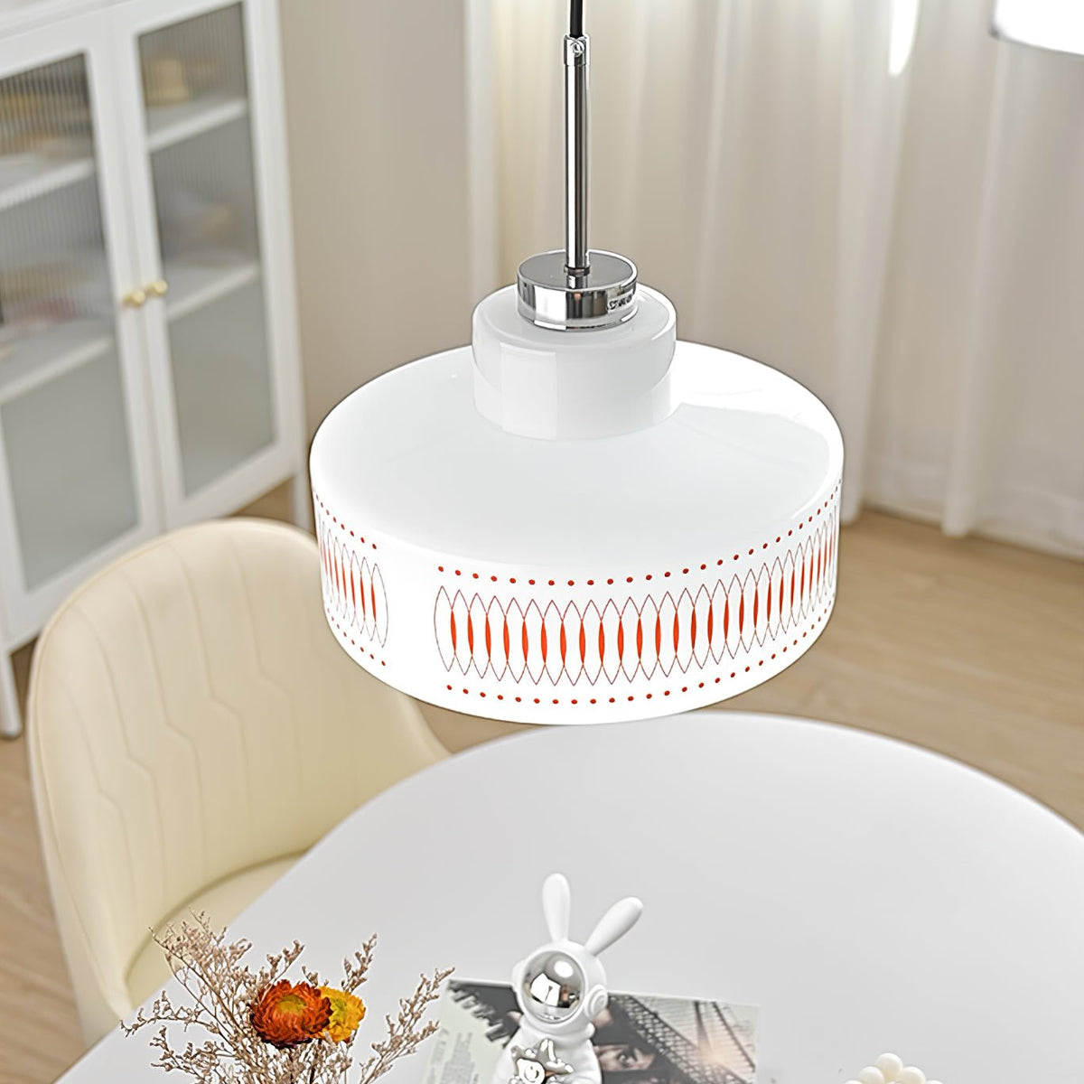 Low angle on a Clérachic pendant with a white drum shade and orange print, hanging above a white oval table and cream chair.