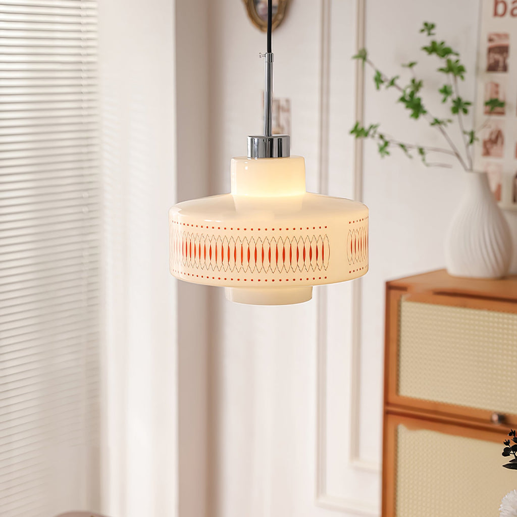 Warm-lit Clérachic pendant with an orange lattice band hangs beside a white vase of leaves and a rattan-fronted cabinet.