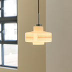 Clérachic pendant with a stepped opal glass shade glows against a cream wall beside a black-framed window.