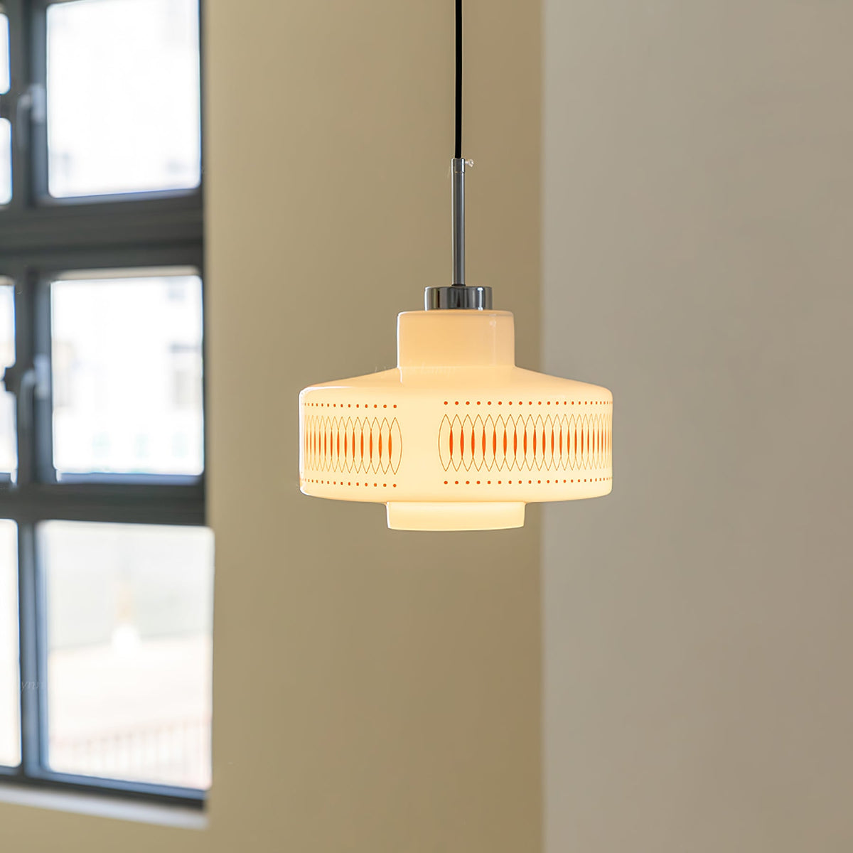 Clérachic pendant with a stepped opal glass shade glows against a cream wall beside a black-framed window.