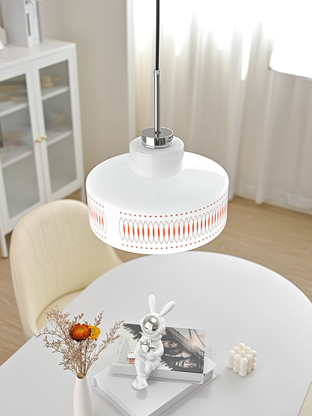 Clérachic pendant with a white printed glass shade hangs above a white round table with a rabbit figure and dried flowers.