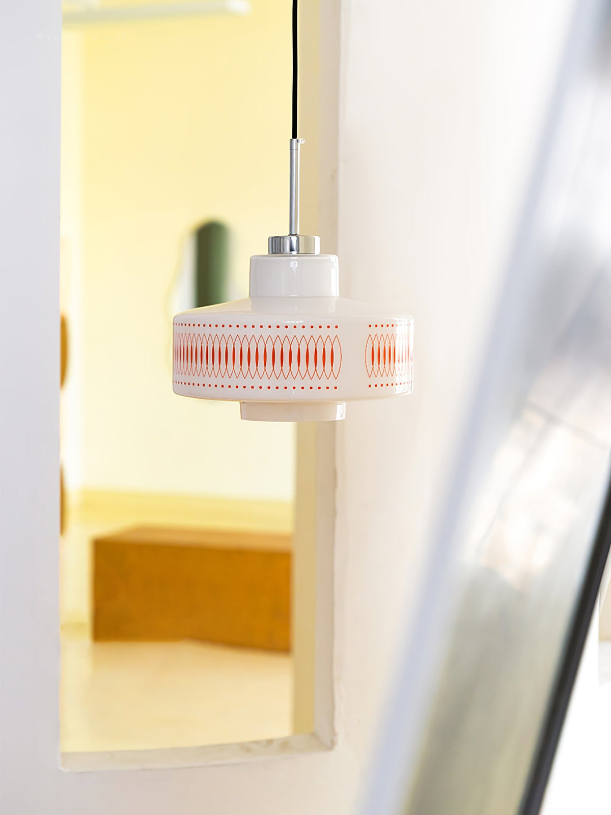 A Clérachic pendant with an orange-printed glass shade hangs beside an open doorway and a mirror, softly lit.