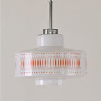 Close view of this Clérachic pendant's white glass shade, orange lattice print and chrome stem against a grey wall.