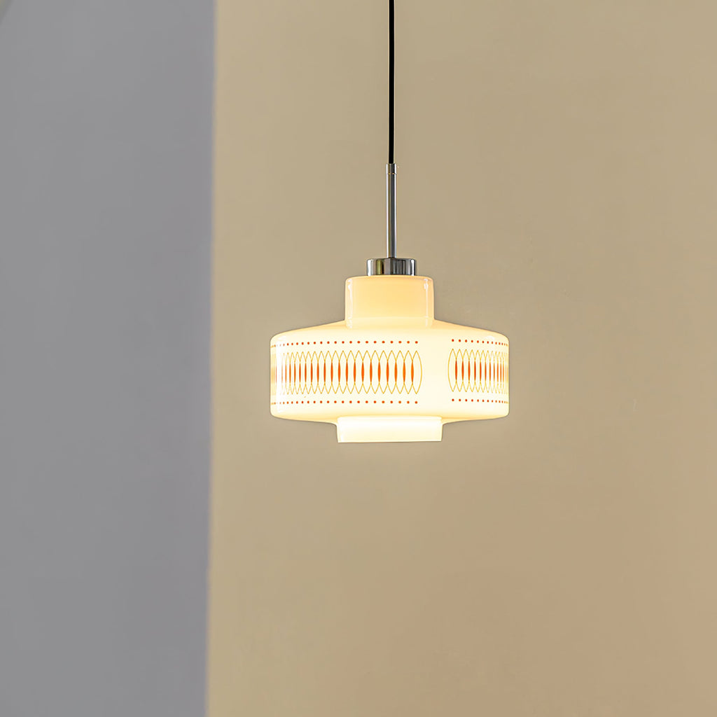 A Clérachic opal glass pendant glows yellow-warm against a tan wall, its orange lattice print softly visible.