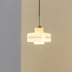 A Clérachic opal glass pendant glows yellow-warm against a tan wall, its orange lattice print softly visible.