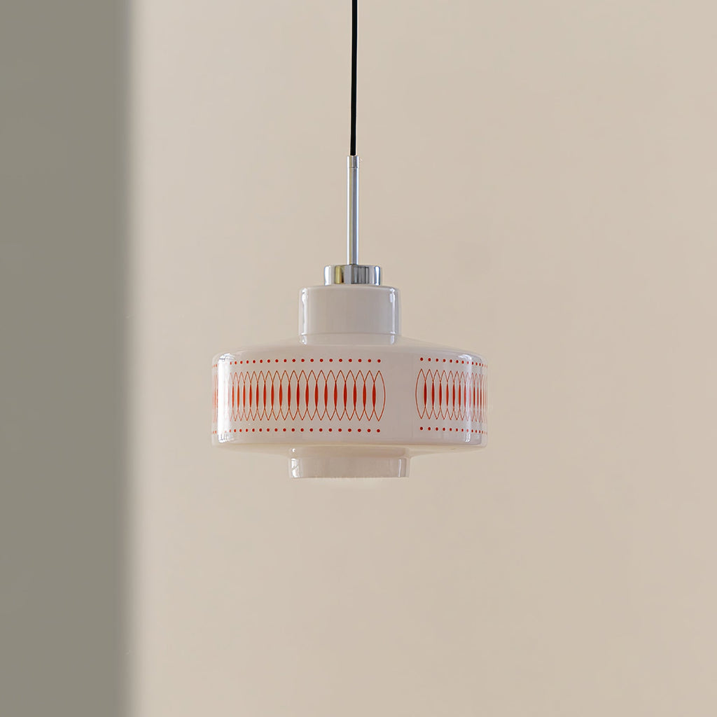 Clérachic pendant with a white glass shade, orange lattice print and a chrome stem, hung against a tan and grey wall.