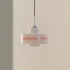 Clérachic pendant with a white glass shade, orange lattice print and a chrome stem, hung against a tan and grey wall.