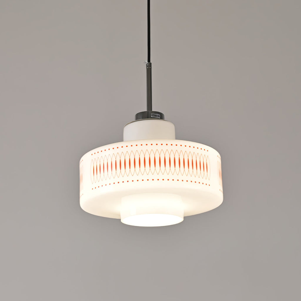 Front view of this Clérachic pendant in white opal glass, its orange lattice and dot print sharp against a grey wall.