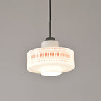 Front view of this Clérachic pendant in white opal glass, its orange lattice and dot print sharp against a grey wall.