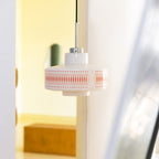 A Clérachic pendant with an orange-printed glass shade hangs beside an open doorway, with a warm yellow room beyond.