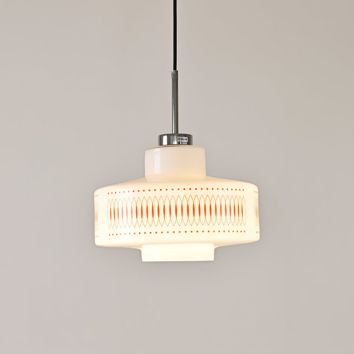 Clérachic pendant with an orange lattice band on a glowing opal shade, hung against a pale grey wall.