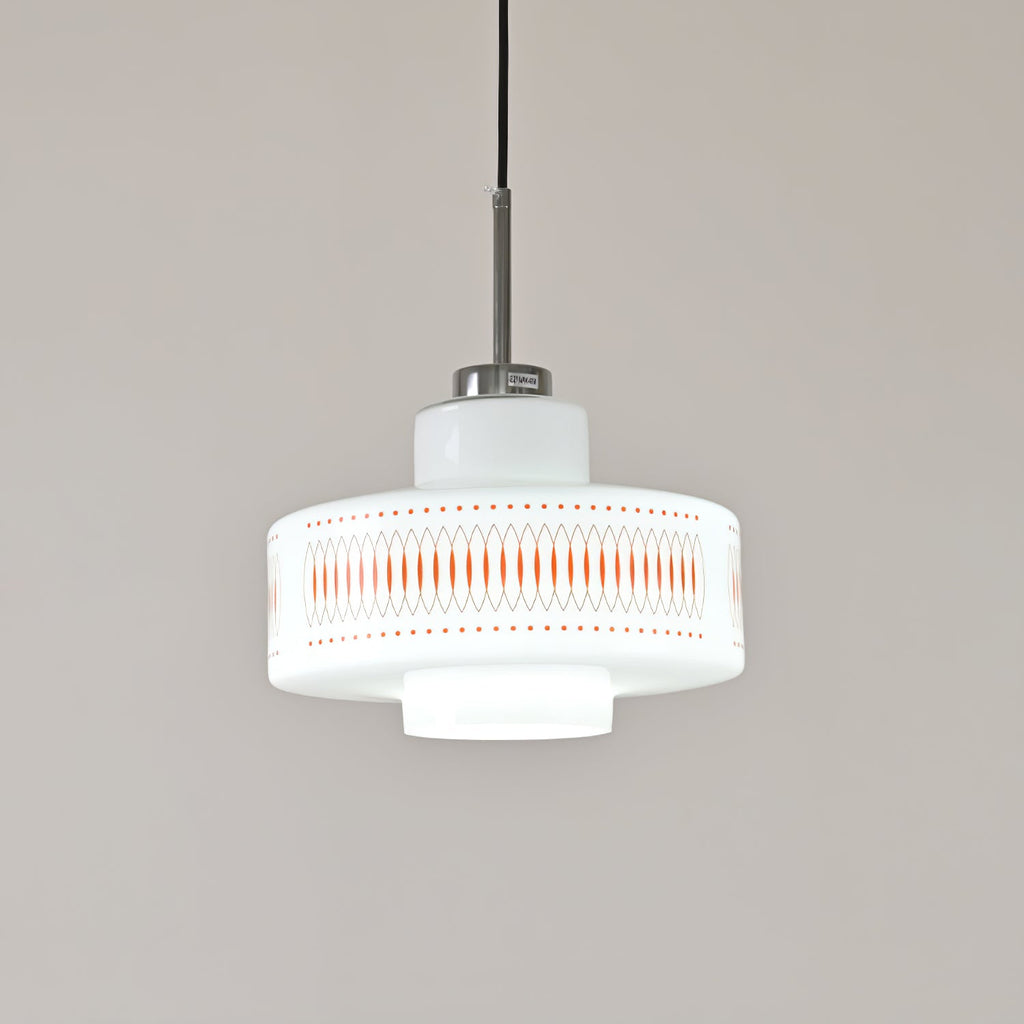 A Clérachic pendant in white opal glass with orange diamond print, shown in cool white light against a grey wall.