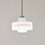 A Clérachic pendant in white opal glass with orange diamond print, shown in cool white light against a grey wall.
