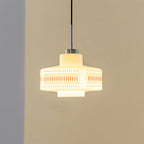 Clérachic pendant with a glowing white glass shade and an orange lattice band, hung against a tan wall with a grey corner.