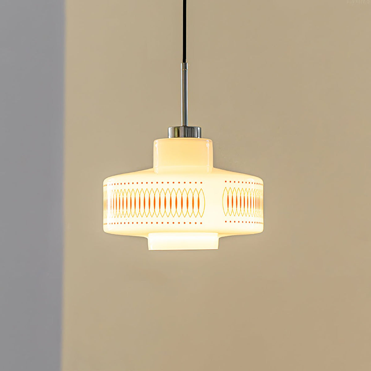 Clérachic pendant with a glowing white glass shade and an orange lattice band, hung against a tan wall with a grey corner.