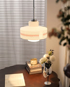 Clérachic pendant with a printed opal shade glows above a dark round table with a book, a vase of white flowers and a pearl strand.