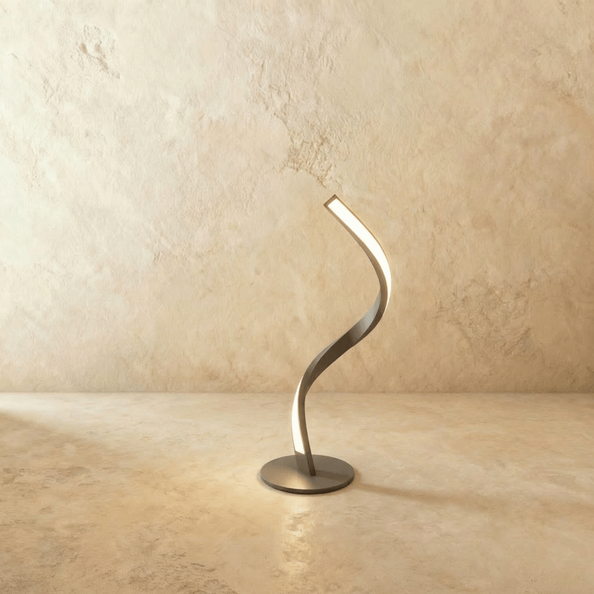 Clérachic spiral LED table lamp in brushed silver-toned metal on a round base, glowing warm on a limewash backdrop.