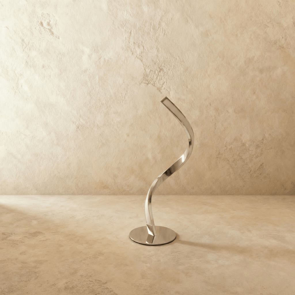 Clérachic chrome-finish spiral table lamp switched off, its mirror-polished ribbon curve and round base on a limewash backdrop.