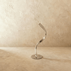Clérachic chrome-finish spiral table lamp switched off, its mirror-polished ribbon curve and round base on a limewash backdrop.