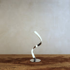 Clérachic spiral LED table lamp with a lit ribbon curve and polished chrome round base, set on a rustic wooden tabletop.