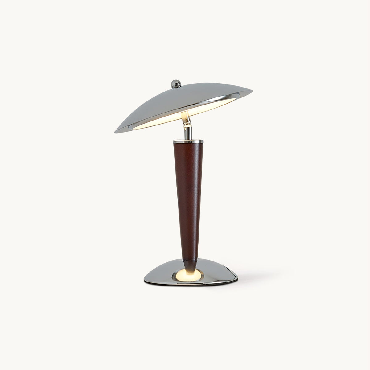 Lit table lamp from Clérachic with a polished chrome dome shade, a tapered walnut-toned wood stem and a chrome base, on a plain white backdrop.