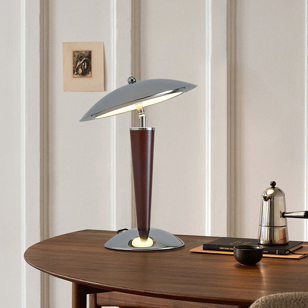 Angled view of a Clérachic chrome dome lamp on a curved walnut table, with a stovetop coffee pot and a small dark bowl beside it.